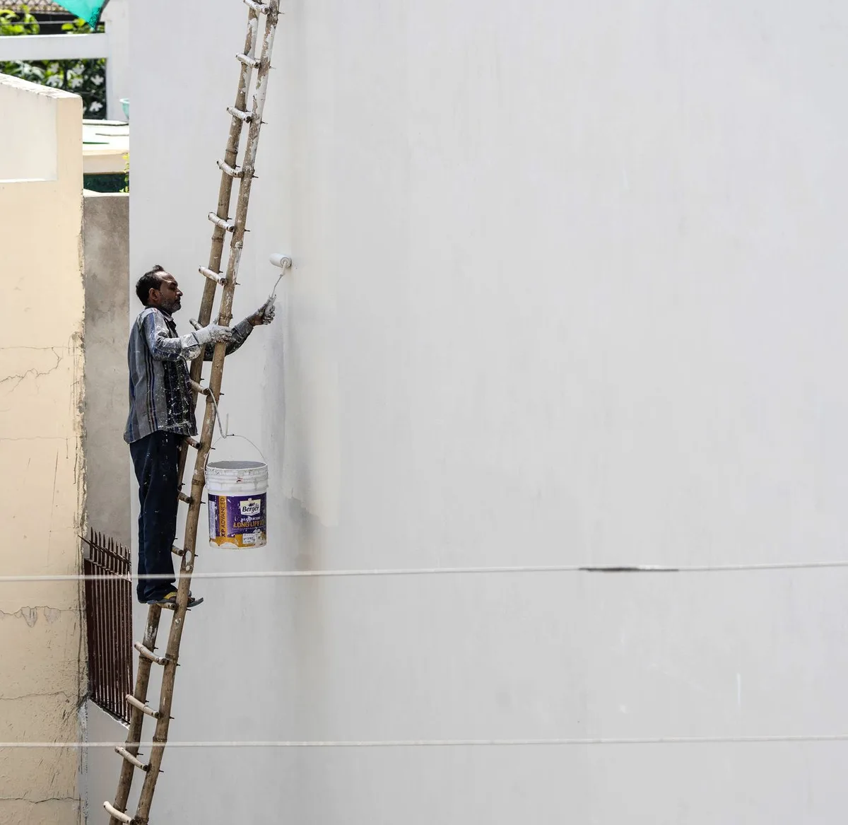 Painter on a ladder rolling paint on a house exterior wall